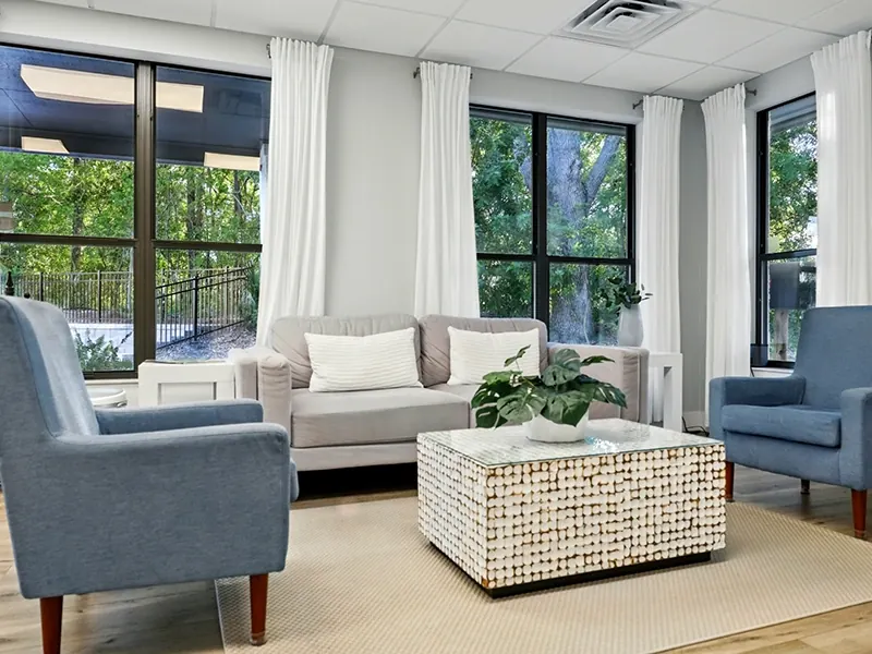 The waiting room at Ponte Vedra Family Dentistry, with blue armchairs, a sofa and tall windows onto the trees.