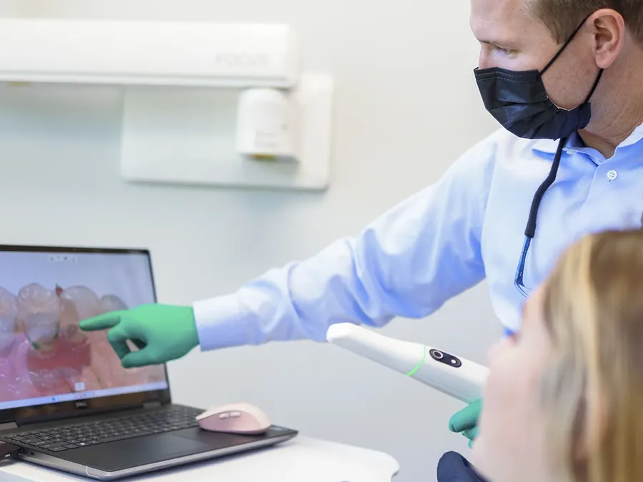 Dr. Perry scanning a patient's teeth with a handheld intraoral scanner, the 3D model appearing on the laptop.